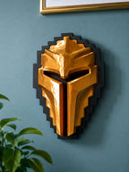 A Tibia Golden Helmet wall sculpture mounted on a textured blue wall, framed by a gold picture frame at the top and green leaves at the bottom left.