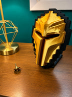 A Tibia Golden Helmet display stand on a wooden table next to a gold geometric lamp, set against a teal wall.